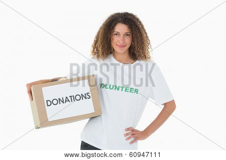 Happy volunteer holding a box of donations with hand on hip on white background