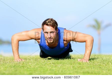 Push-ups - fitness man training push up outside in grass in summer. Fit male athlete working out cross training exercising outdoor. Caucasian muscular sports model in his 20s.