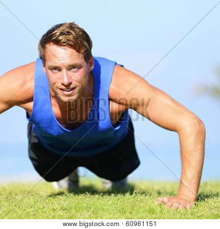 Push ups - fitness man exercising push up outside in grass in summer. Fit male athlete working out cross training outdoor. Caucasian muscular sports model in his 20s.
