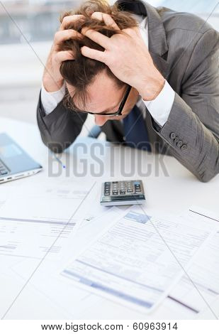 tax, business and stress concept - stressed businessman with papres, laptop and calculator