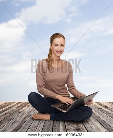 happiness, internet, technology and people concept - smiling young woman sitting on floor with laptop computer