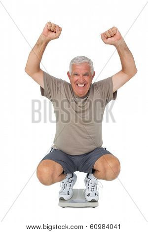 Full length portrait of a senior man cheering on weight scale over white background