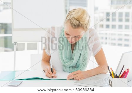 Casual young woman writing notes in a bright office