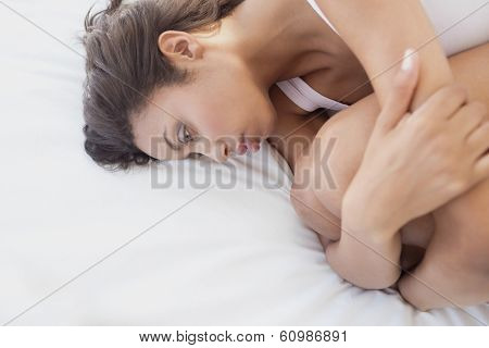 Sad brunette lying on bed holding her knees at home in the bedroom