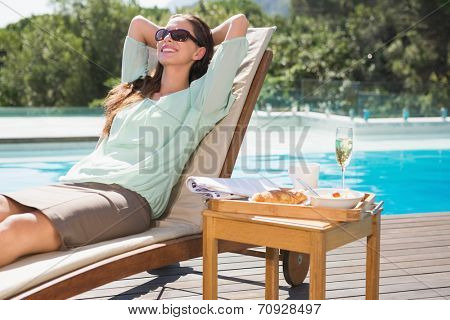 Beautiful young woman relaxing by swimming pool with breakfast on table