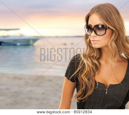 people, tourism and travel concept - beautiful young woman in shades over summer beach and boat background