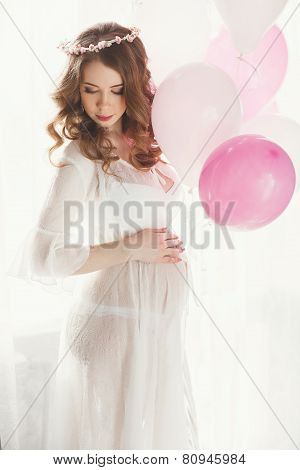 Pregnant woman in a white nightgown with balloons.