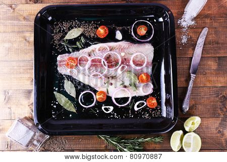 Pangasius fillet with spices and vegetables on firepan and wooden table background