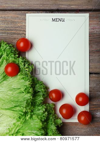 Menu sheet of paper with cherry tomatoes and lettuce on rustic wooden surface background
