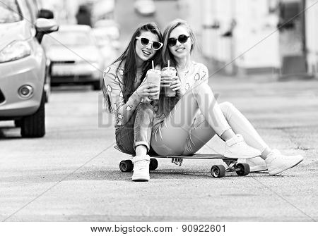 Beautiful young girls hipster girlfriends posing with a skateboard seat on skate, street fashion lif