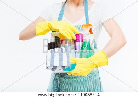 Closeup of cleaning supplies in plactic box holded by young housewife in blue kitchen apron over white background