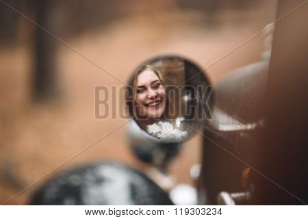 Stylish Loving wedding couple kissing and hugging in a pine forest near retro car