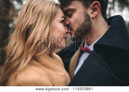 Stylish Loving wedding couple kissing and hugging in a pine forest near retro car