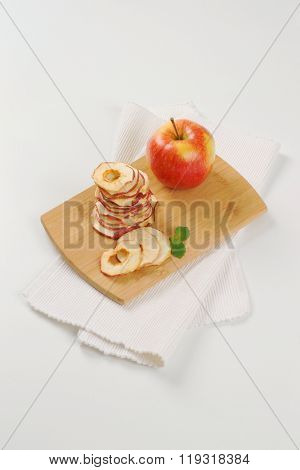 stack of dried apple chips and fresh apple on wooden cutting board