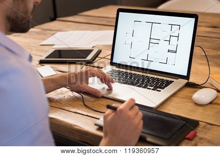 Close up of a young interior designer working in office. Architect working on laptop at new house project with graphics tablet. Interior designer studying layout of his house project on computer.