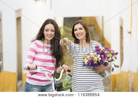 Two beautiful female friends smiling and pointing to somewhere