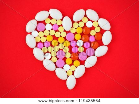 Colorful Tablets Arranged In A Heart Shape On Red Background. Symbol Photo Of Heart Disease, Medicat
