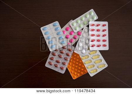 Heap of packs of pills and capsules isolated on brown wooden background