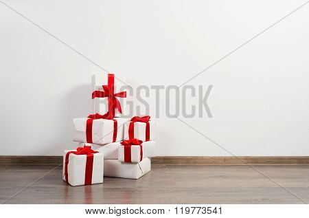 A pile of Christmas gifts in colorful wrapping with ribbons against the wall on a beautiful hardwood floor with copyspace.