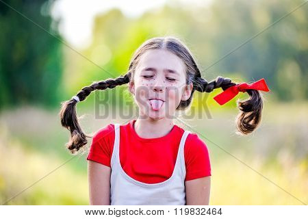 A funny cute outdoor portrait of a little girl presenting Pippi Longstocking and showing out out her tongue.
