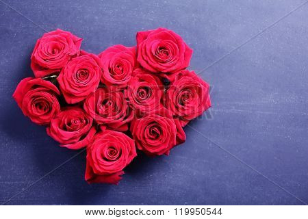 Fresh red roses buds in shape of heart on black textured background