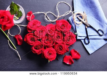 Fresh red roses buds in shape of heart with rope on black textured background