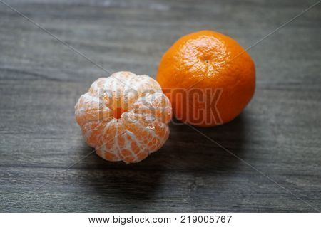 peeled and unpeeled clementines or tangerines or mandarin oranges on rustic wooden background with selective focus