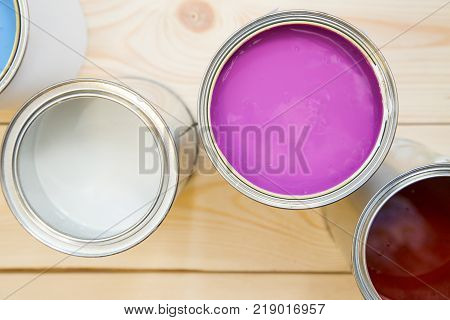 Painting new appartment. Tin cans of fuchsia, white and brown, oil paint on a light uncolored wooden background. Close up. Top view. Space for your text or pruduct display.