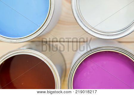 Background with tin cans of blue, white, pink and brown oil paint. on a light uncolored wooden background. Close up. Top view. Space for your text or pruduct display.