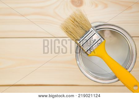 Redecoration tools. A tin can of household white oil paint with brush on top, light uncolored wooden background. Close up. Top view. Space for your text or pruduct display.