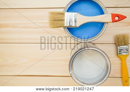 Redecoration tools. Tin cans of paint and wooden brushes, light wooden background. Close up. Top view. Space for your text or pruduct display.