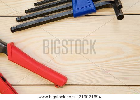 Wooden background with a set of repair tools- hex keys and pilers. Close up. Top view. Space for your text or pruduct display.