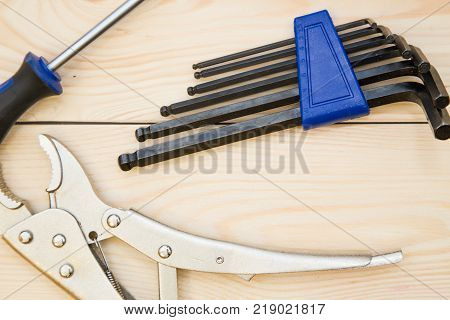 A set of repair tools-pilers, screwdriver and hex keys on a light uncolored wooden background. Close up. Top view. Space for your text or pruduct display.