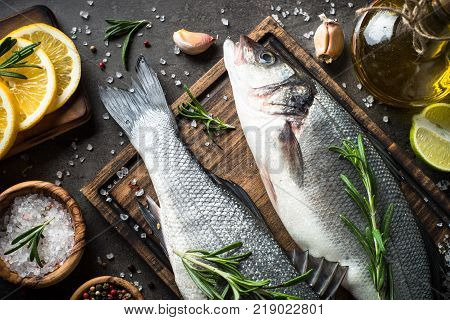 Fresh fish seabass. Uncooked seabass with spices and herbs on black slate table. Top view.