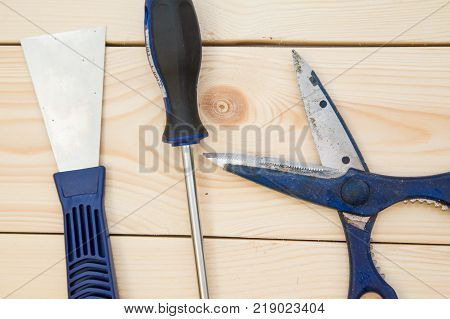 Repairing and construction concept. A set of tools for house repair-a plastering trowel, scissors and screwdriver on a light uncolored wooden background, close up. Top view. Space for your text or pruduct display.