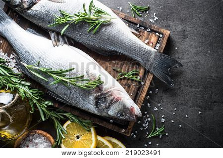 Fresh fish seabass. Raw fish seabass with spices and herbs on black slate background. Top view with copy space.