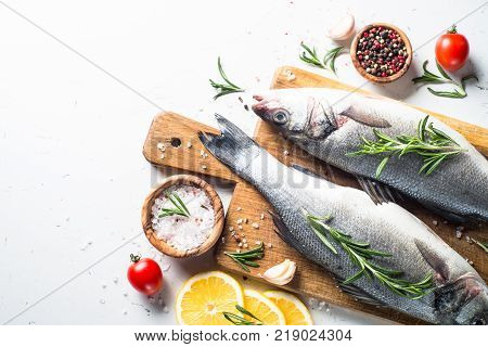 Fresh fish seabass. Raw fish seabass with spices and herbs ingredients for cooking on white background. Top view with copy space.
