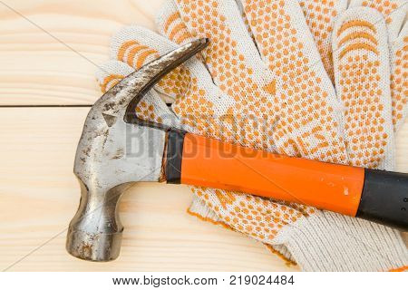 Repairing and construction concept. Tools for house repair- a hammer and a pair of protective work gloves on a light uncolored wooden background, close up. Top view. Space for your text or pruduct display.