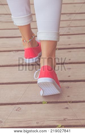Detail of female feet in sneakers while walking on a wooden post.
