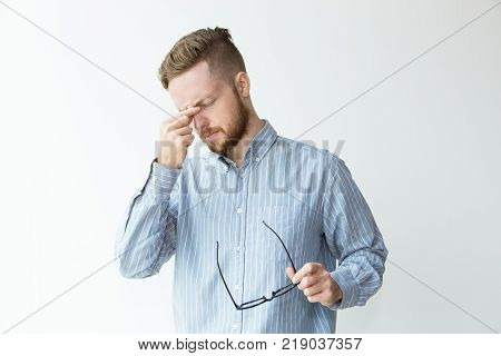Portrait of tired young man with closed eyes and hand keeping on bridge of nose. Businessman taking off glasses after long working day. Work balance concept.