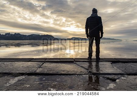 Man standing at the beach in the Norwegian fjord Tovdalsfjorden, looking at the calm sea and the mist and fog. Hamresanden, Kristiansand, Norway