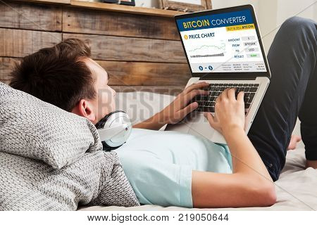 Man using Bitcoin converter website to trade bitcoin price while rest on the bed.