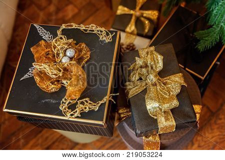 Black paper gift boxes with golden ribbon bow near the Christmas tree. Classic christmas and New Year decorated interior room with presents and New year tree.