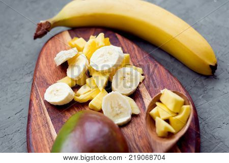 pieces of mango fruit and banana on the wooden cutting board on concrete background