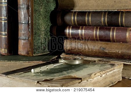 An ancient book in a ragged cover and a magnifying glass on a table closeup on a blurred background of other old books
