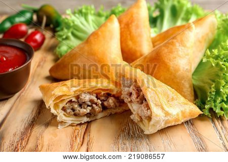 Wooden board with delicious meat samosas, closeup