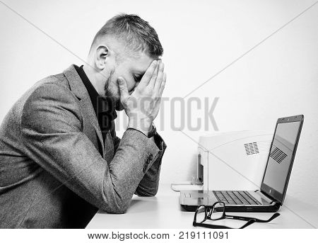 a tired man with his hands on the his face at the table with a laptop in the office. black and white.