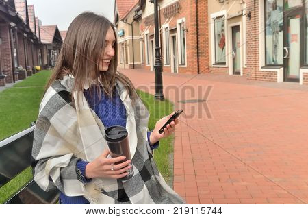 A smiling woman is sitting on a bench wrapped in a plaid holds a thermocouple in her hands and a phone sits side by side with the photographer