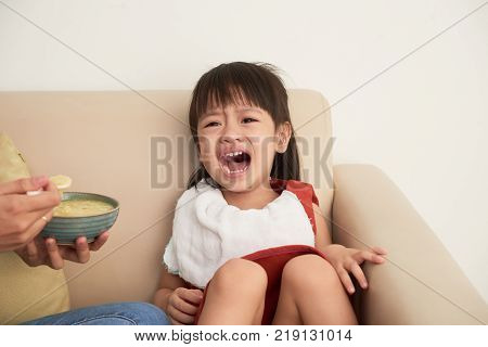 Crying Asian little girl does not want to eat soup