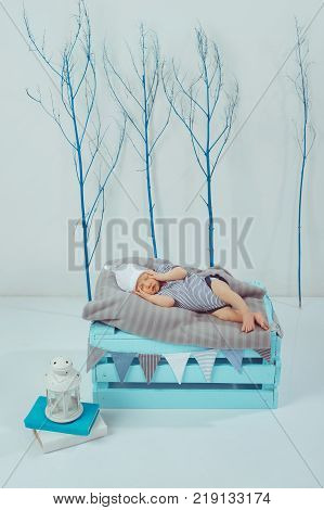 adorable newborn baby in bodysuit and hat sleeping on wooden box with lantern near by